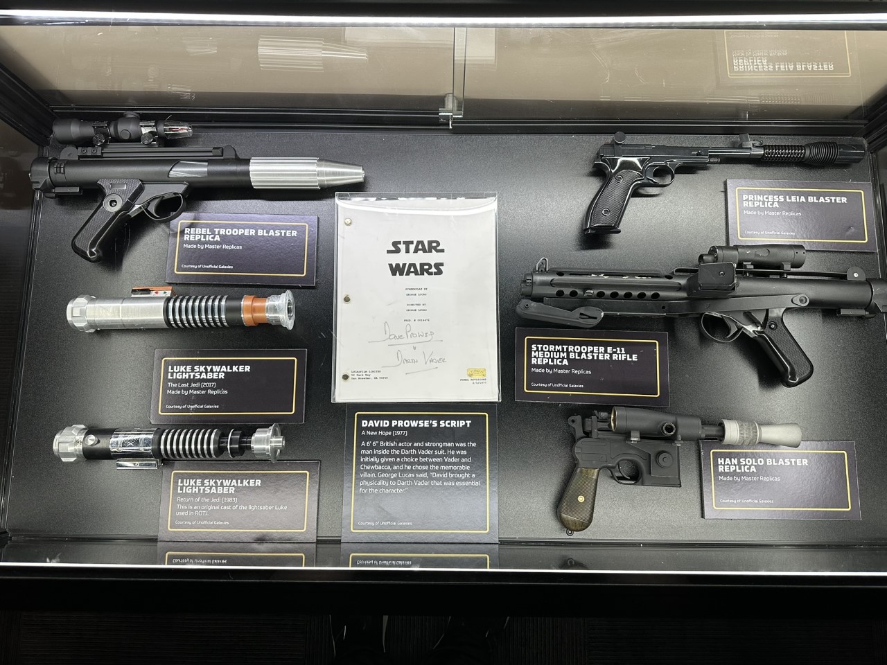 Display case of Star Wars weapon replicas including lightsabers and blasters with David Prowse's signed script